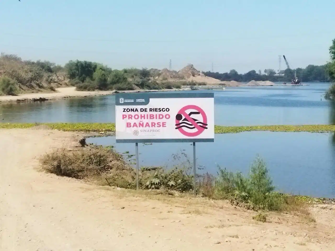 Rótulo anunciando zona de riesgo (prohibido bañarse) en el área de un río en Culiacán