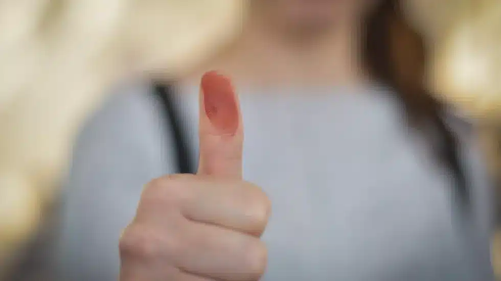 Una persona levanta el dedo pulgar manchado de tinta