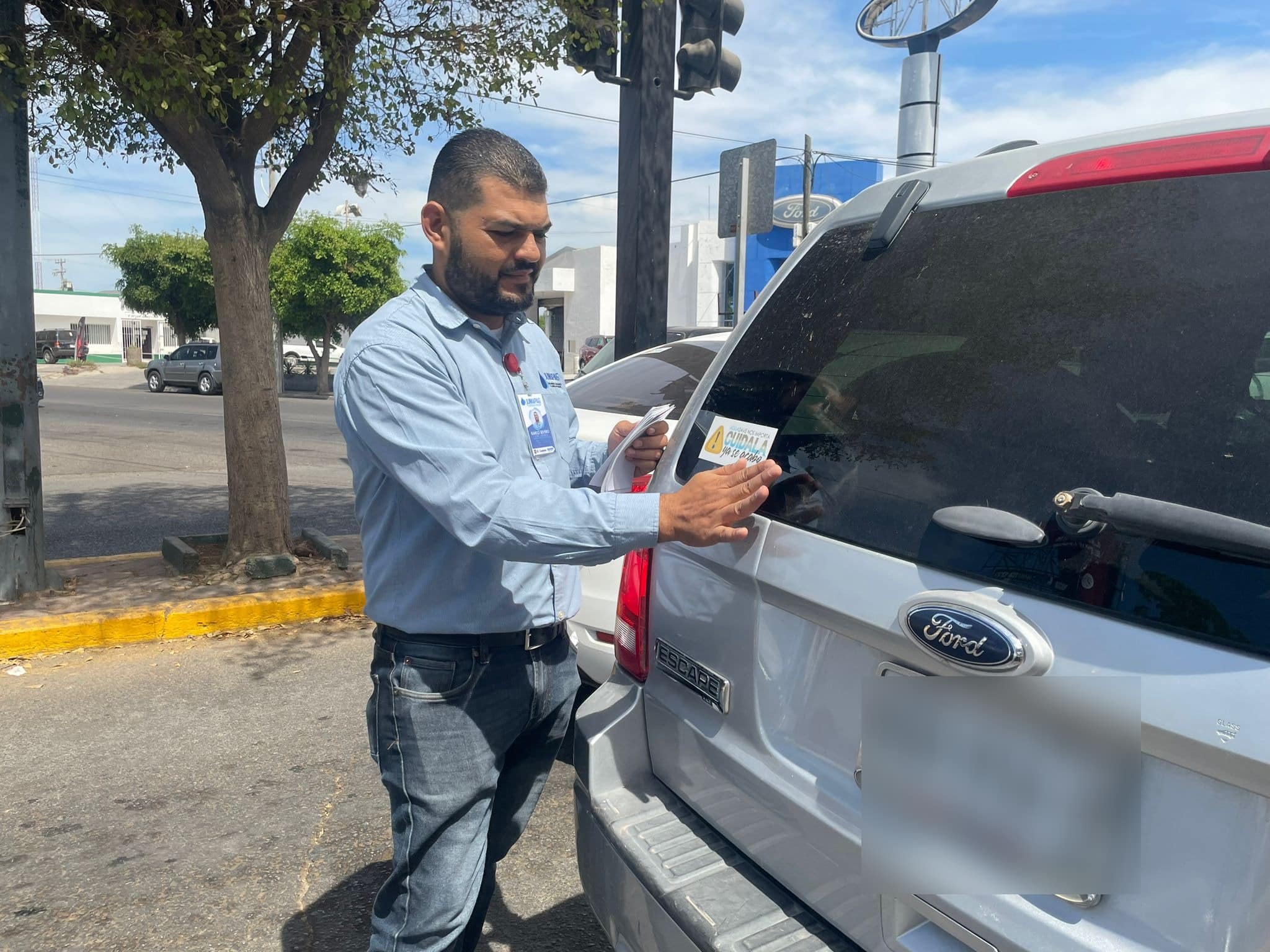 Personal de la Jumapag poniendo calcomanías en los carros en Guasave