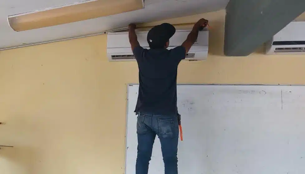 Trabajador instala aire acondicionado tipo minisplit en un salón de clases de educación básica