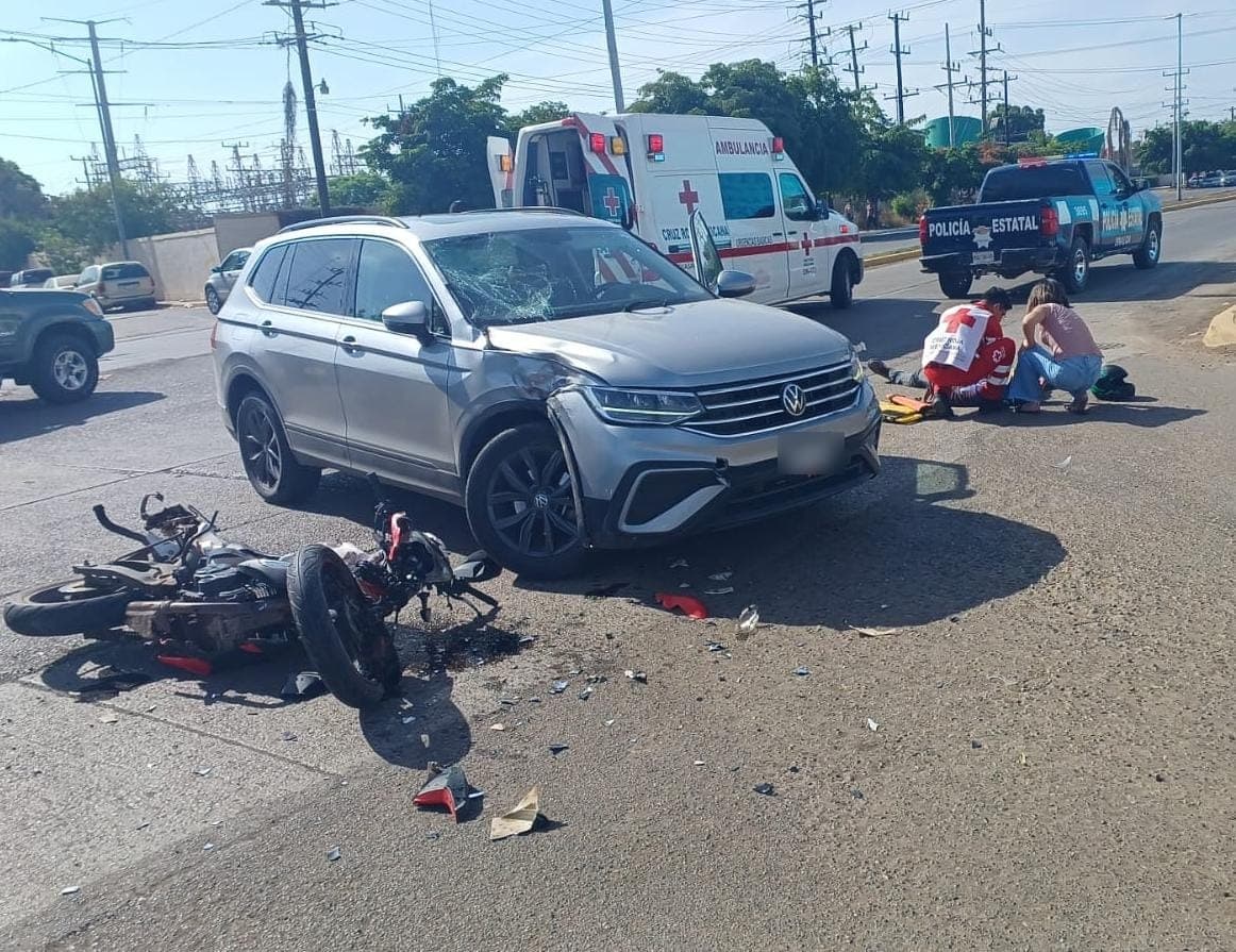 Motocicleta dañada y tirada junto a una camioneta con un daños en un costado. Paramédicos auxilian al lesionado