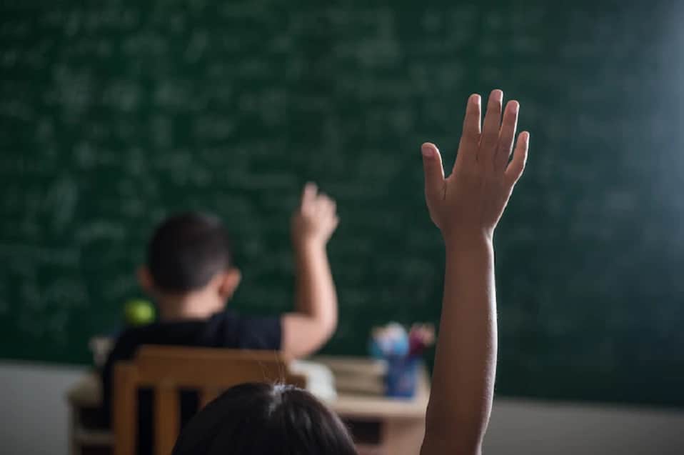 Alumnos levantando la mano en salón de clases