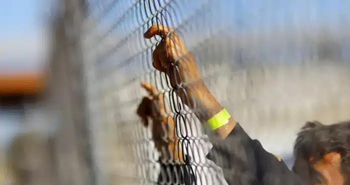Migrante sostiene a una valla en la frontera de EU y México