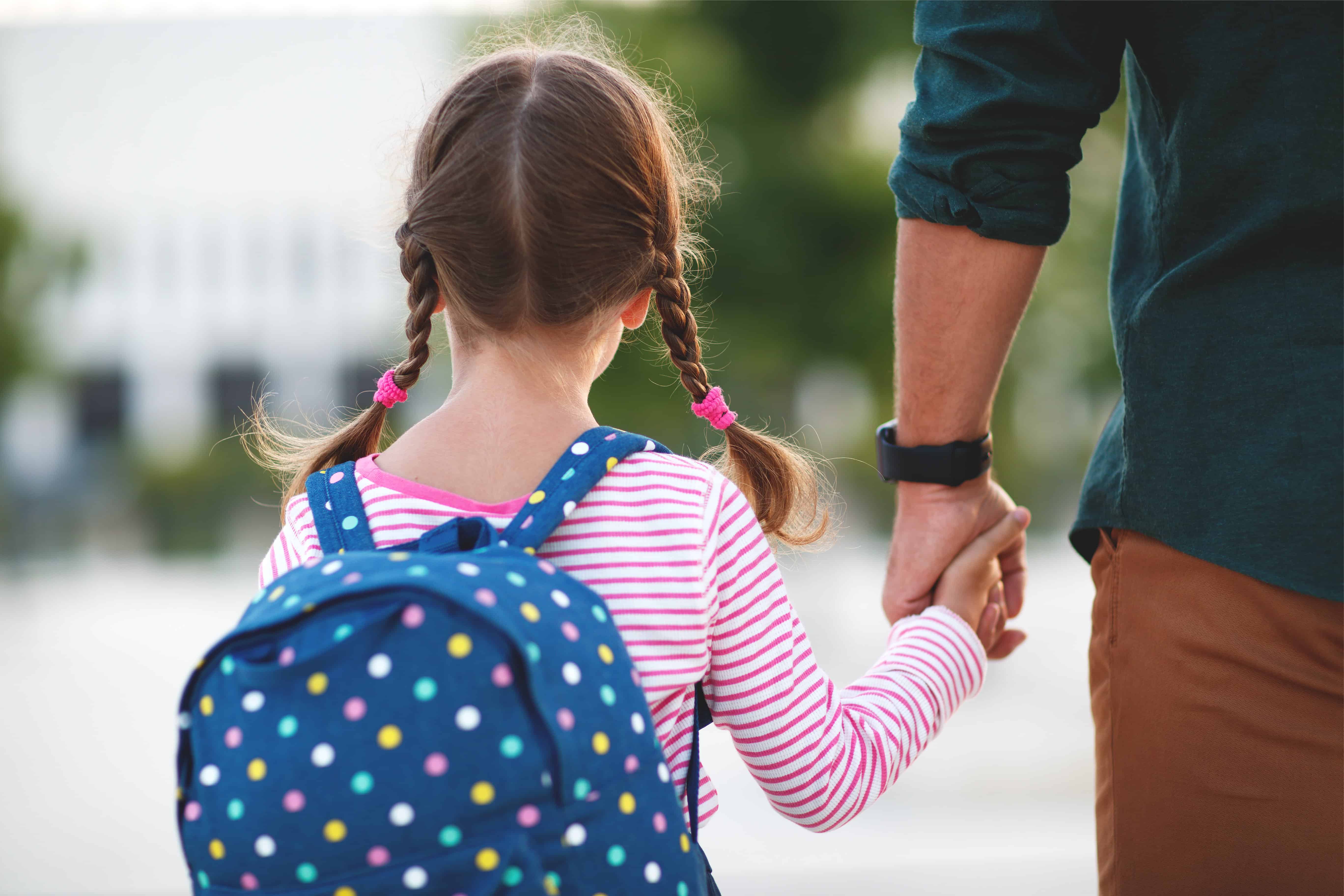 Niña con mochila sosteniendo la mano de su padre