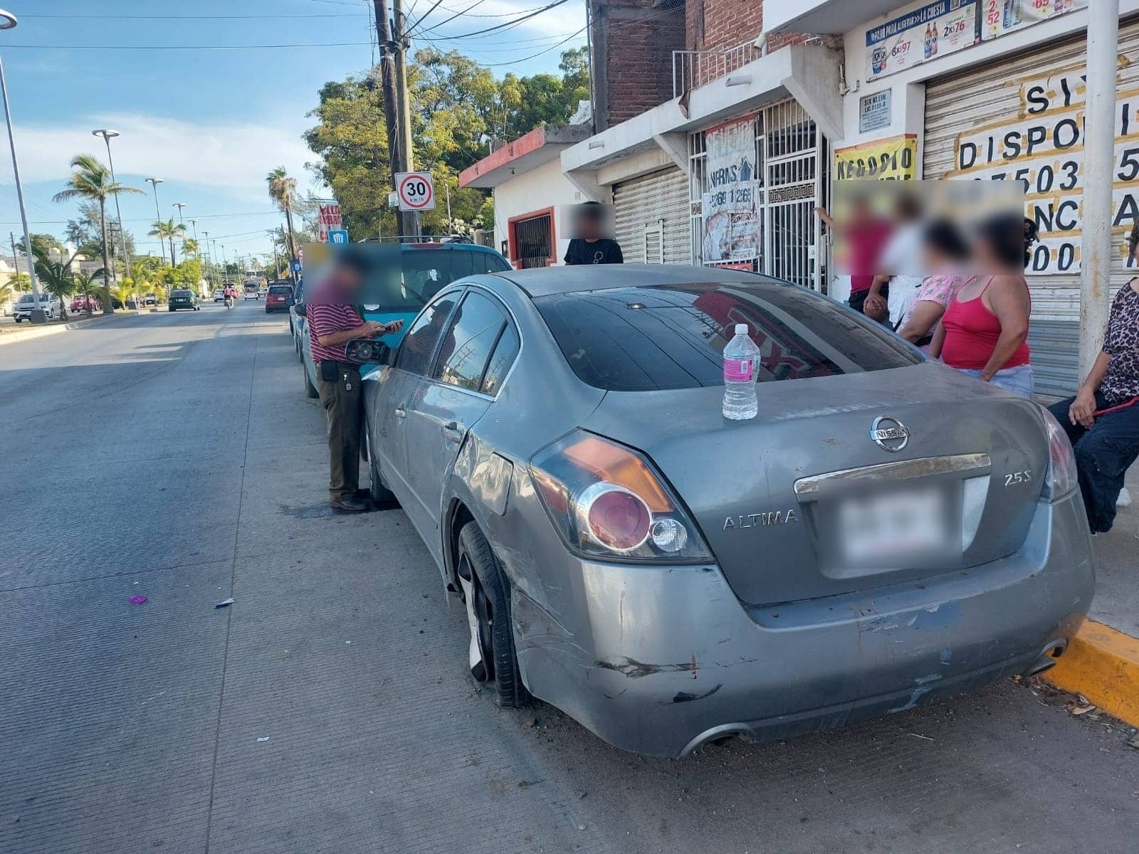 Vehículo gris con daños por choque y personas en el lugar