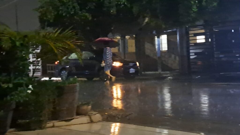 Persona caminando por la noche lluviosa en Guasave sosteniendo un paraguas