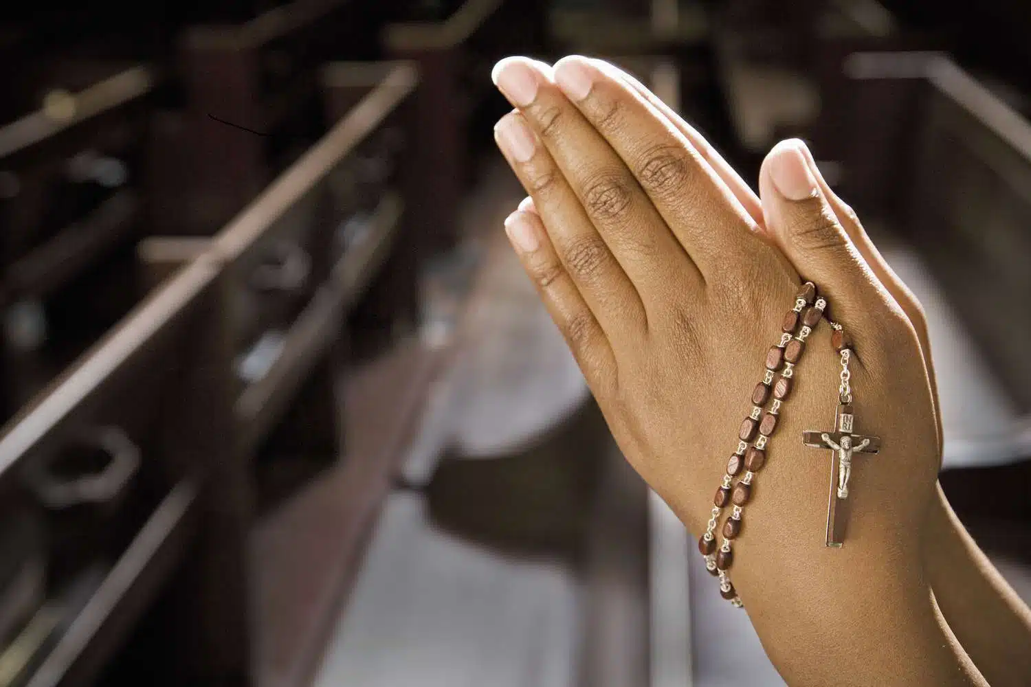 Manos sosteniendo un rosario al interior de una iglesia