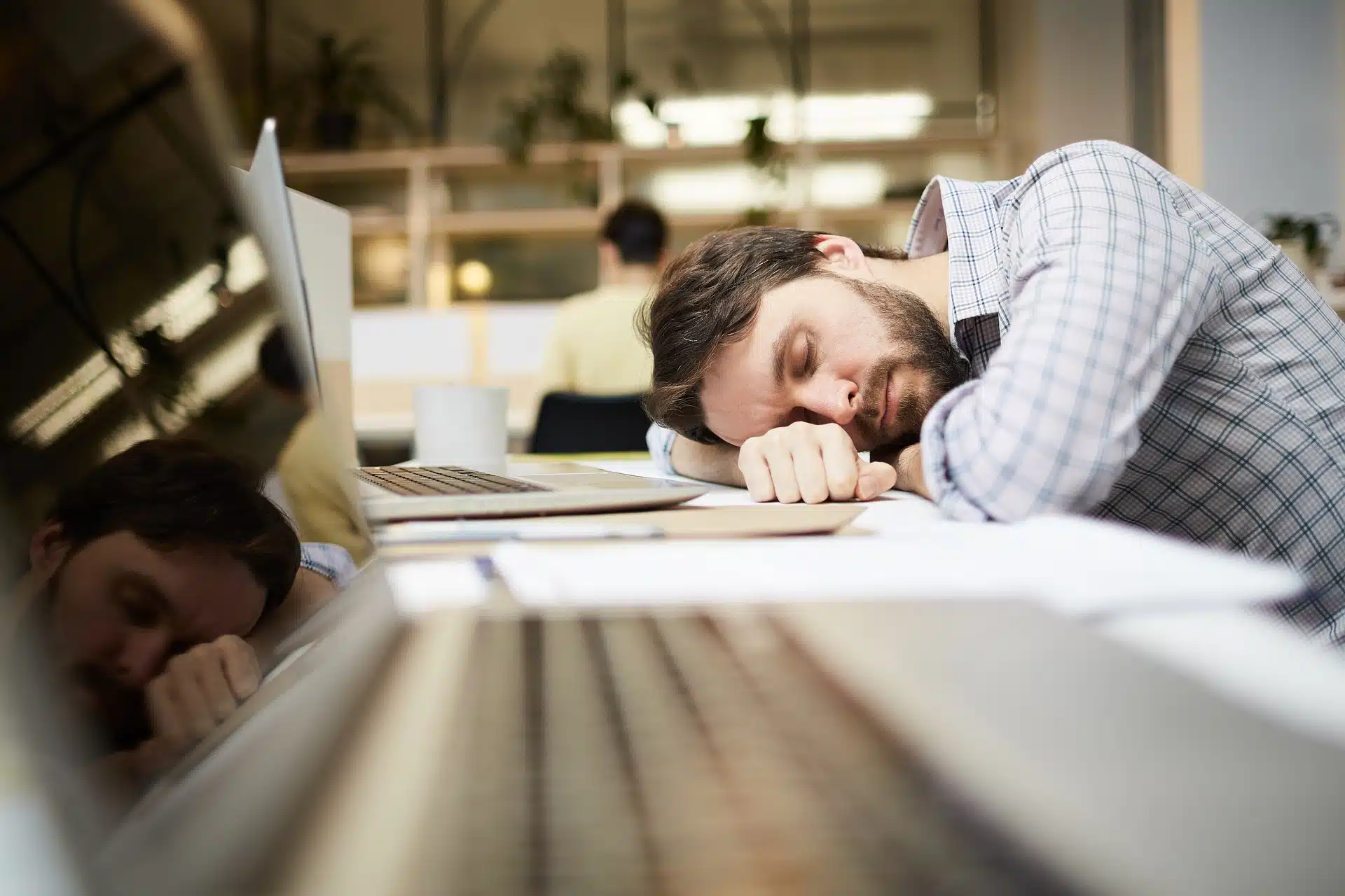 Hombre vestido formal recostado sobre un escritorio en una oficina con síndrome de burnout o cansacio por una larga jornada laboral
