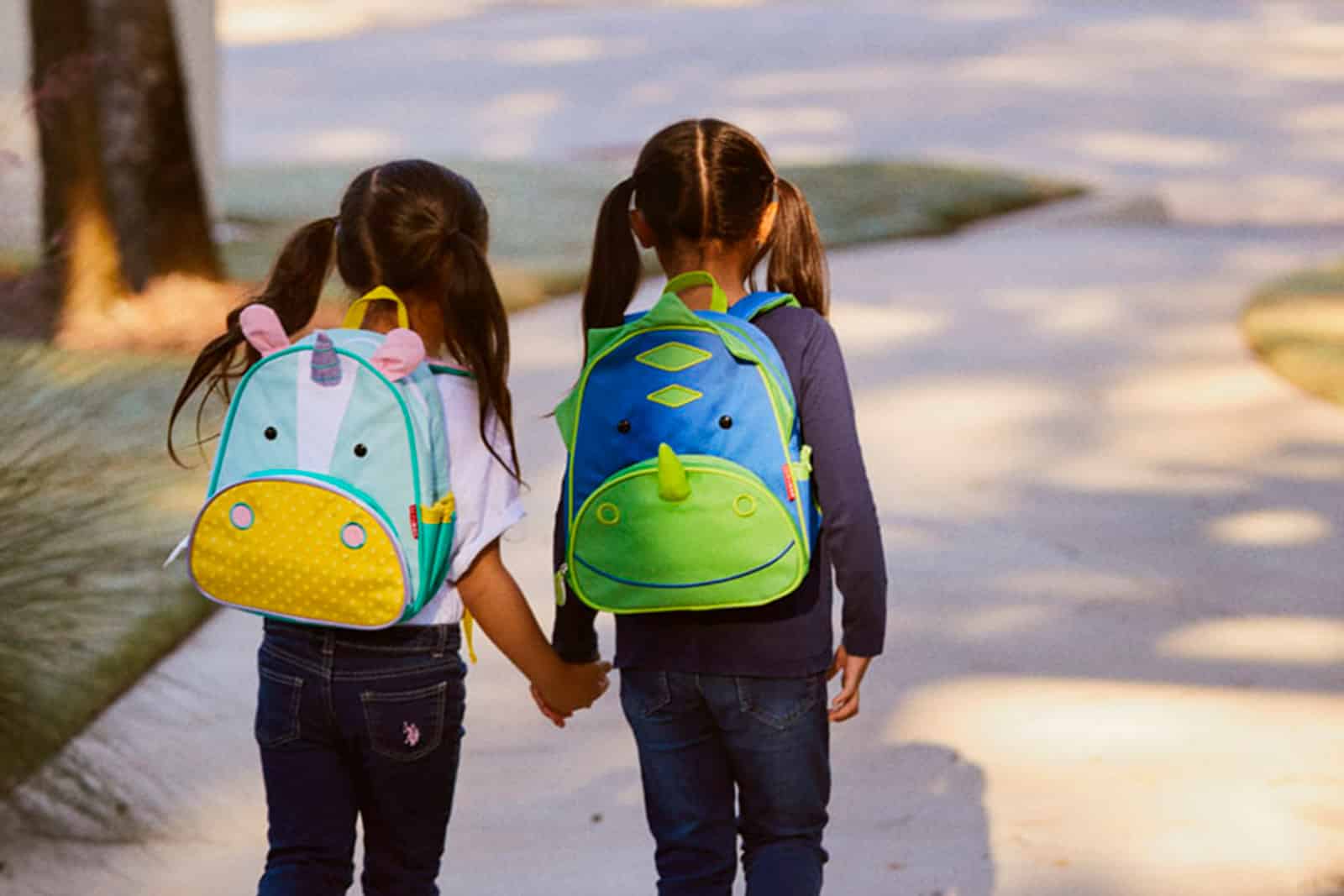 Niñas caminando tomadas de la mano con mochilas de dibujos animados