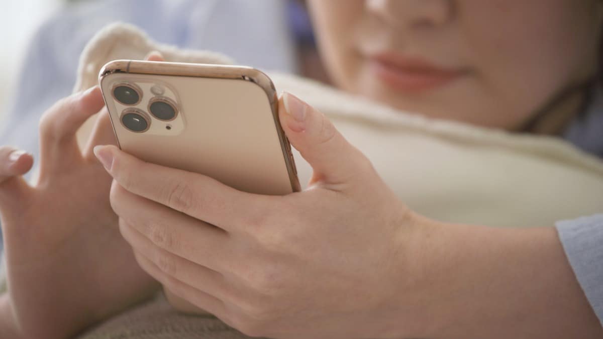 Una mujer sosteniendo un celular en sus manos mientras teclea la pantalla.