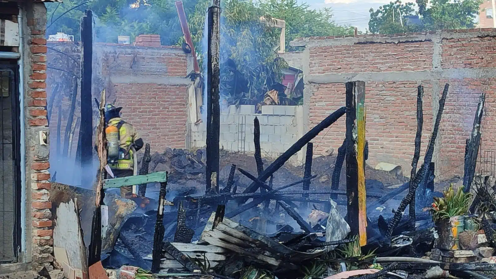 Bomberos sofocando el incendio en la vivienda completamente dañada.