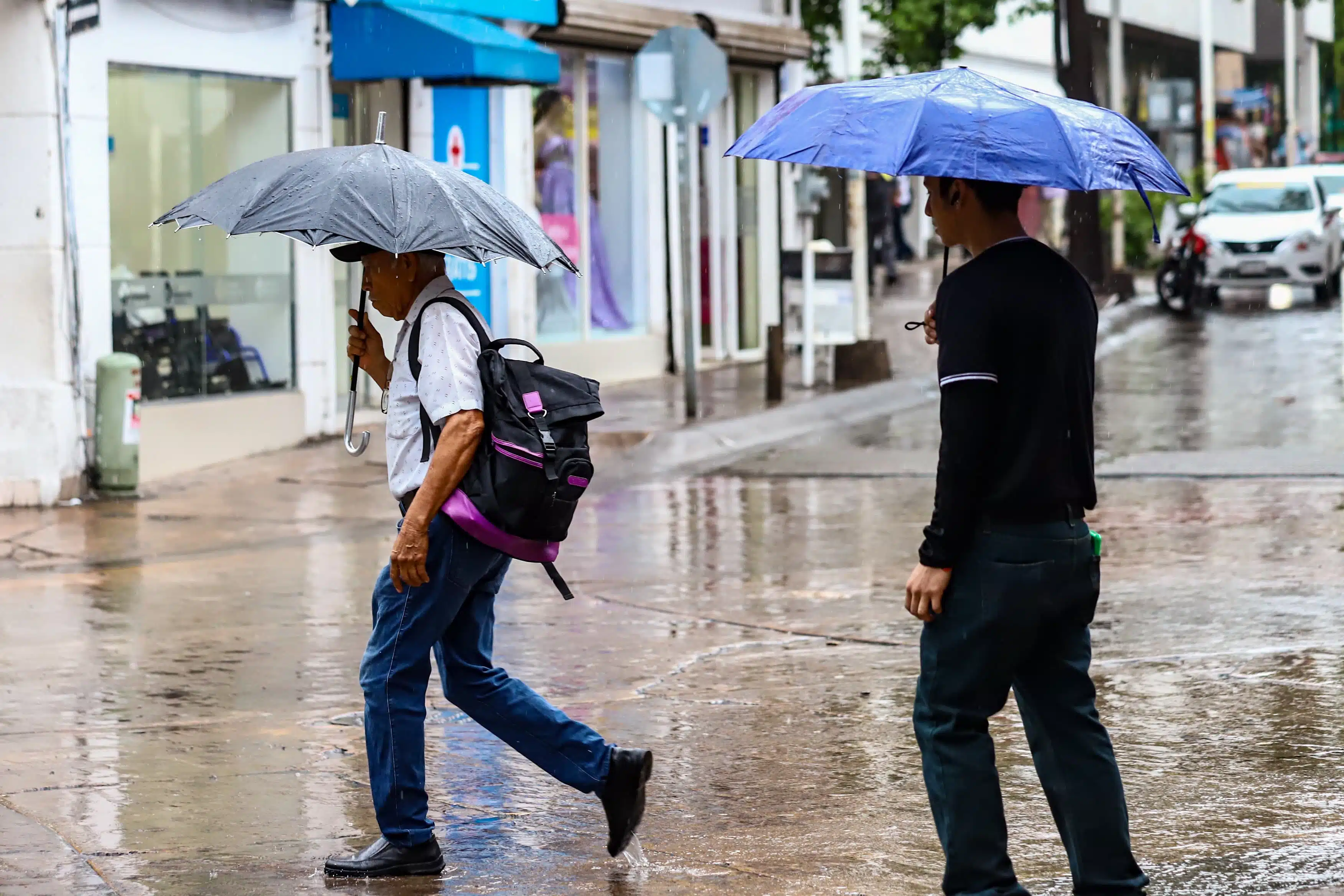 Personas cubriéndose con una paraguas de la lluvia cuando cruzan por calle encharcada