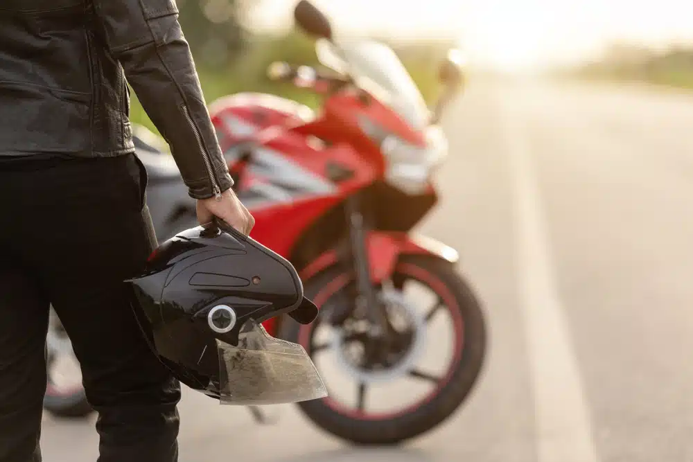 Motociclista sosteniendo su casco con la mano al lado de una carretera.