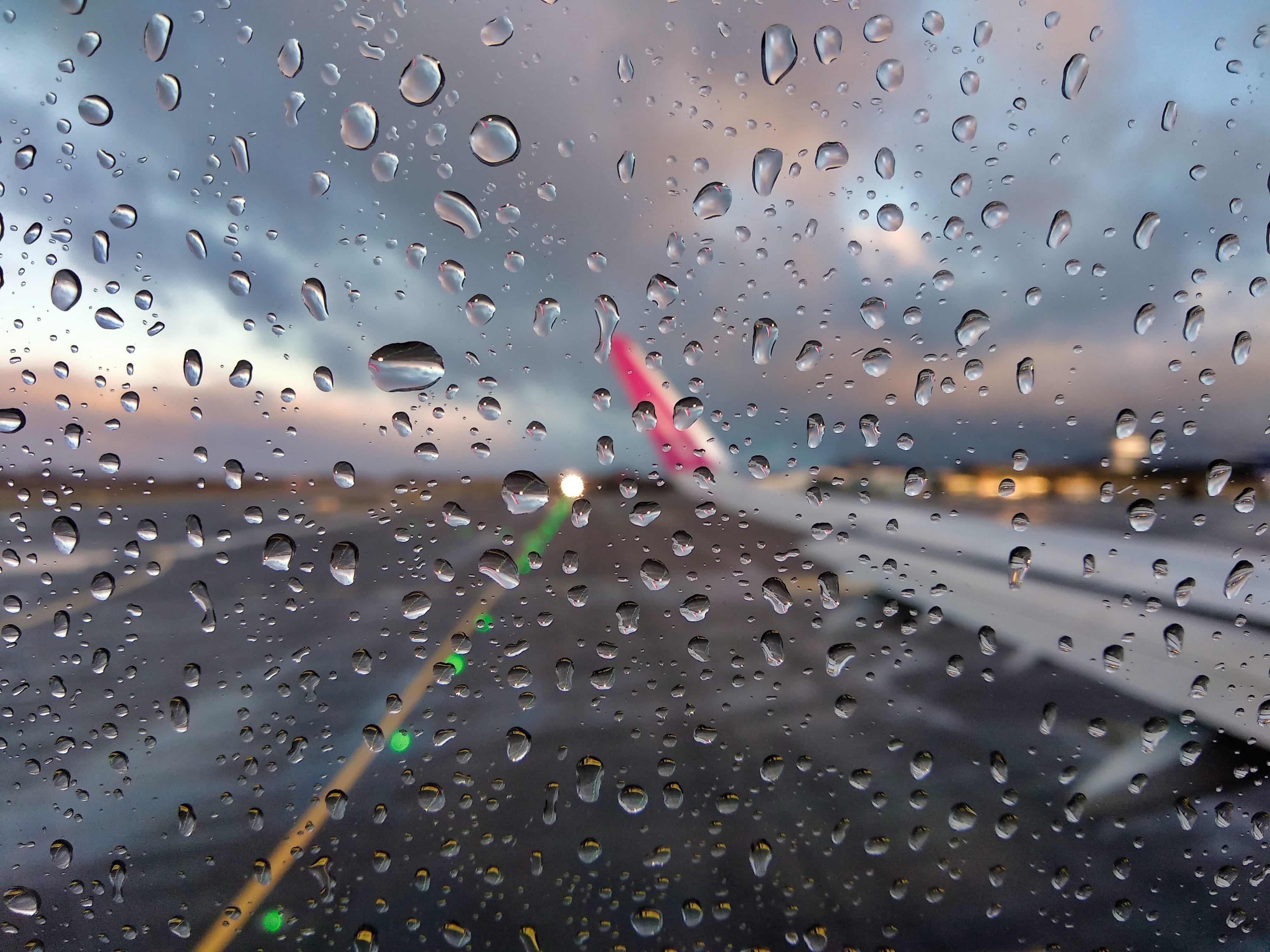 Una vista borrosa de la pista de un aeropuerto a través de la ventana de un avión con gotas de lluvia
