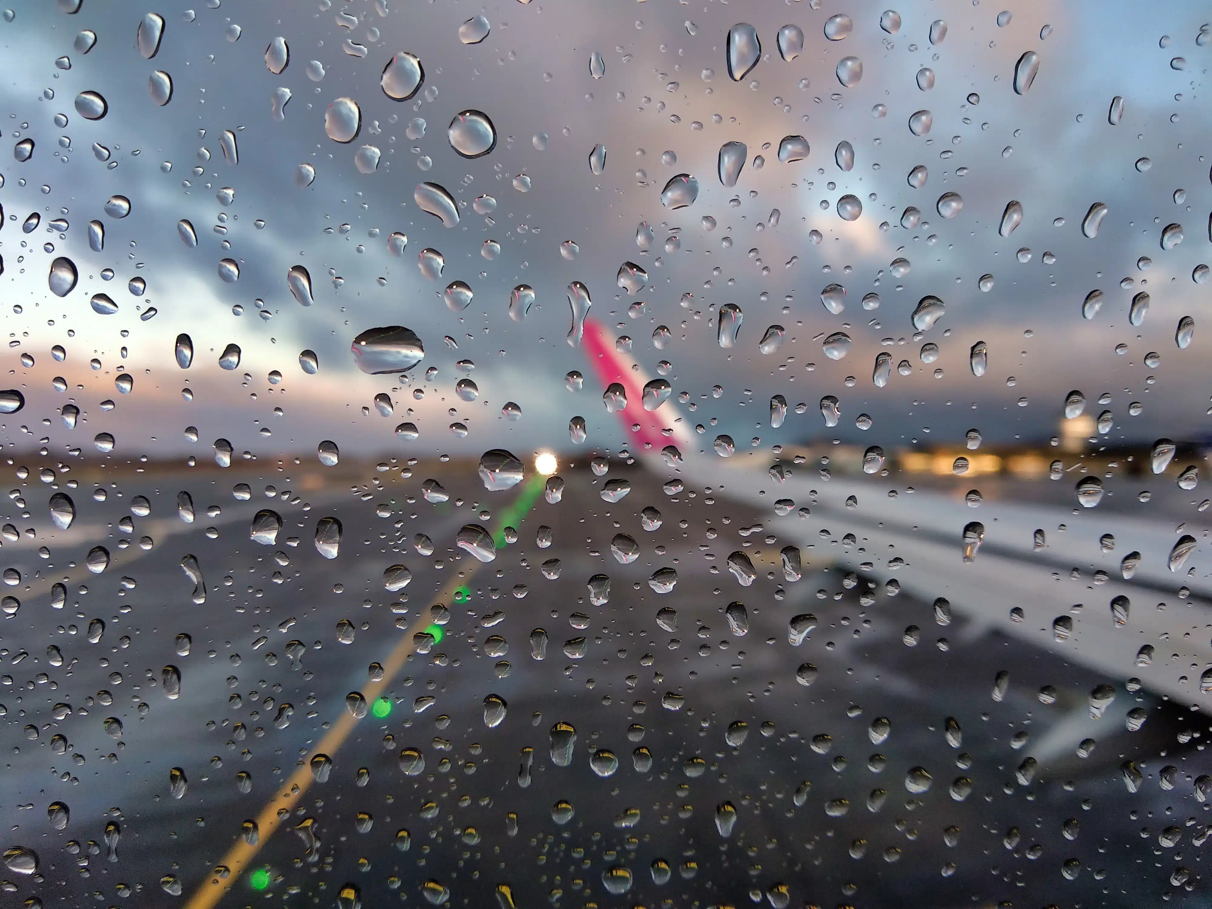 Una vista borrosa de la pista de un aeropuerto a través de la ventana de un avión con gotas de lluvia