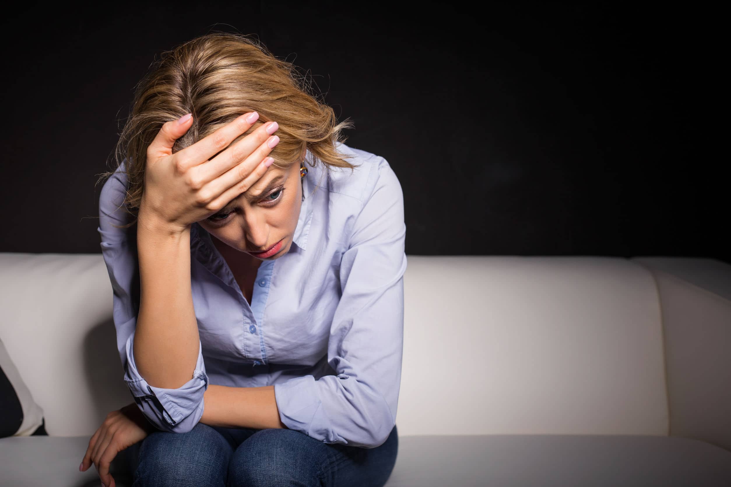 Una mujer sentada en un sofá mientras padece un episodio que afecta su salud mental.