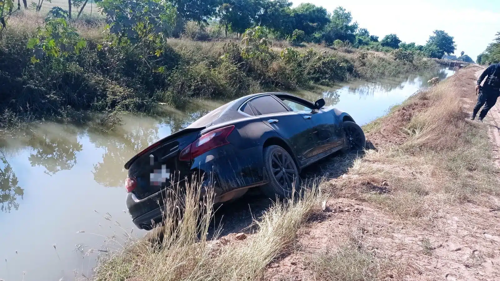 Vehículo Nissan Altima negro abandonado en el borde del canal.