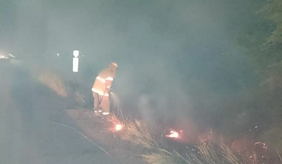 Un bombero apaga el fuego provocado en la maleza, a un lado de la carretera México 15