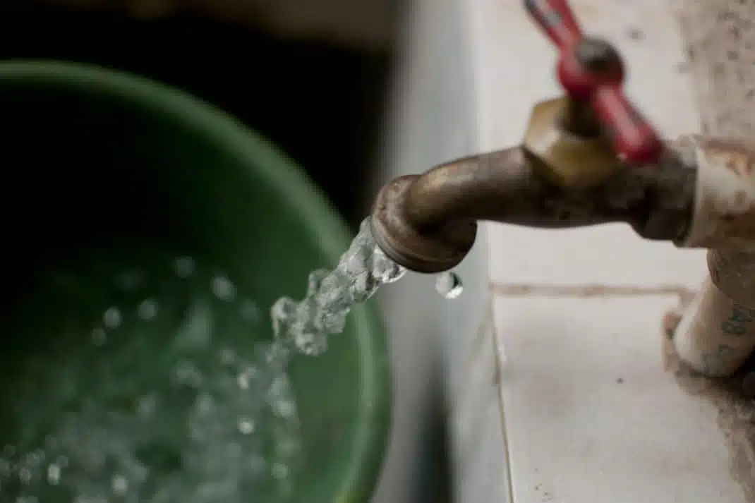 Llave abierta con agua potable que cae a cubeta