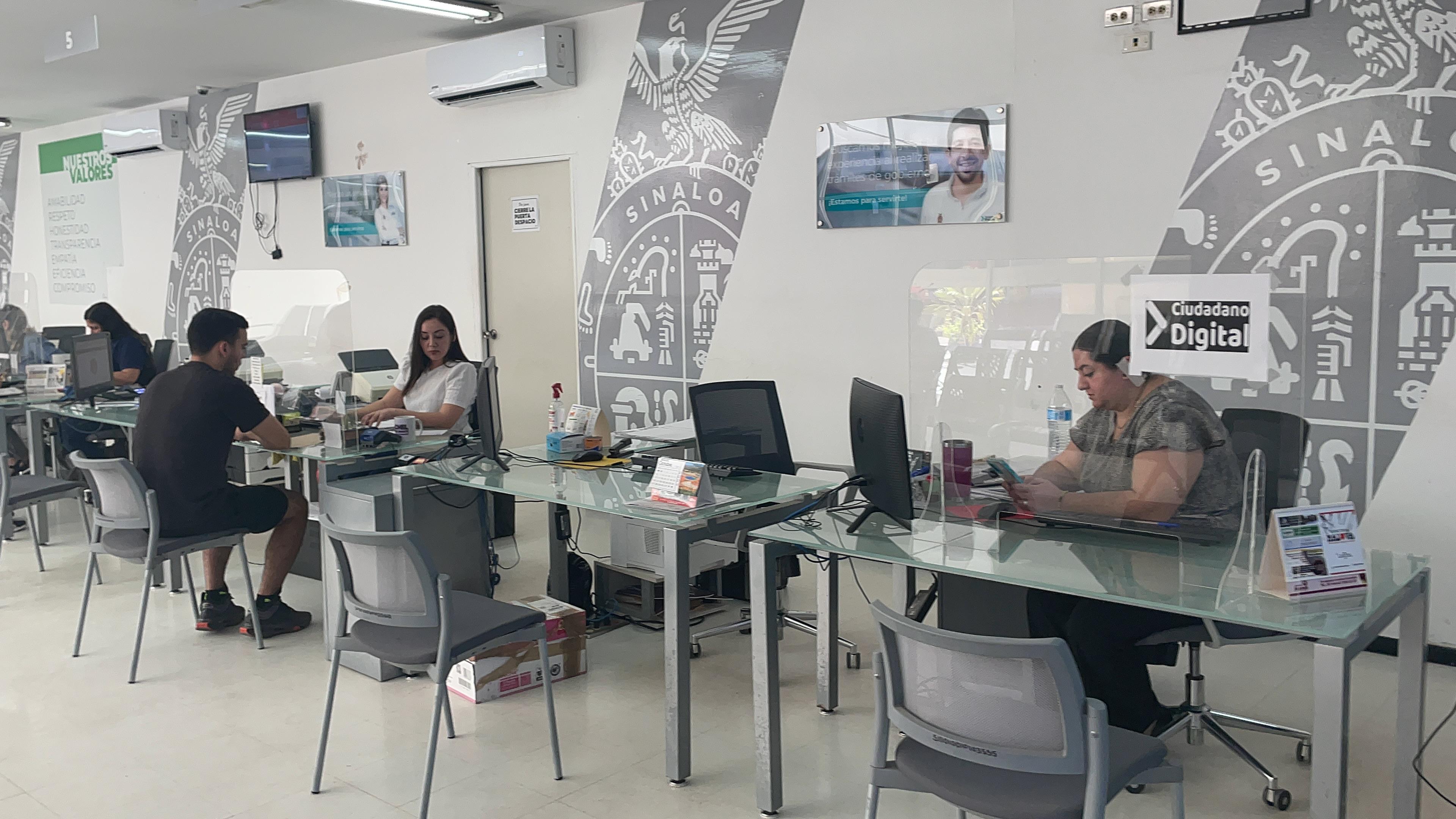 Escritorios con una ventanilla con personas sentadas en una oficina
