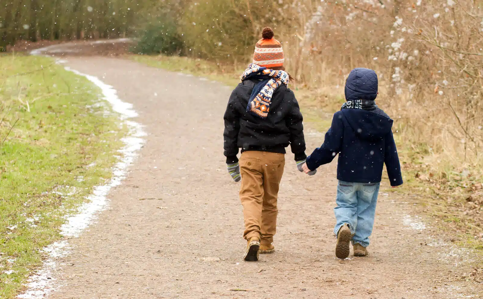 Niños con ropa invernal tomados de la mano y caminando por un espacio verde.