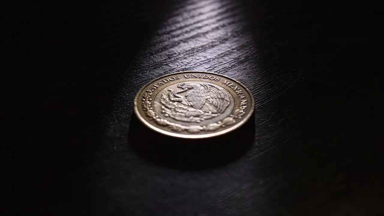 Una moneda con valor de 10 pesos mexicanos sobre una mesa de madera en la oscuridad