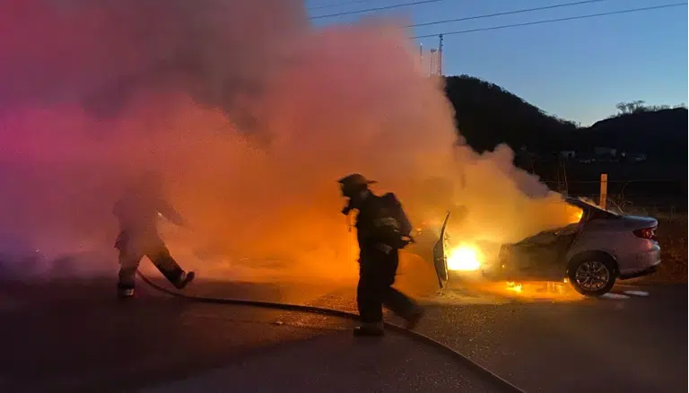 Bomberos intentan apagar el incendio sobre un automóvil