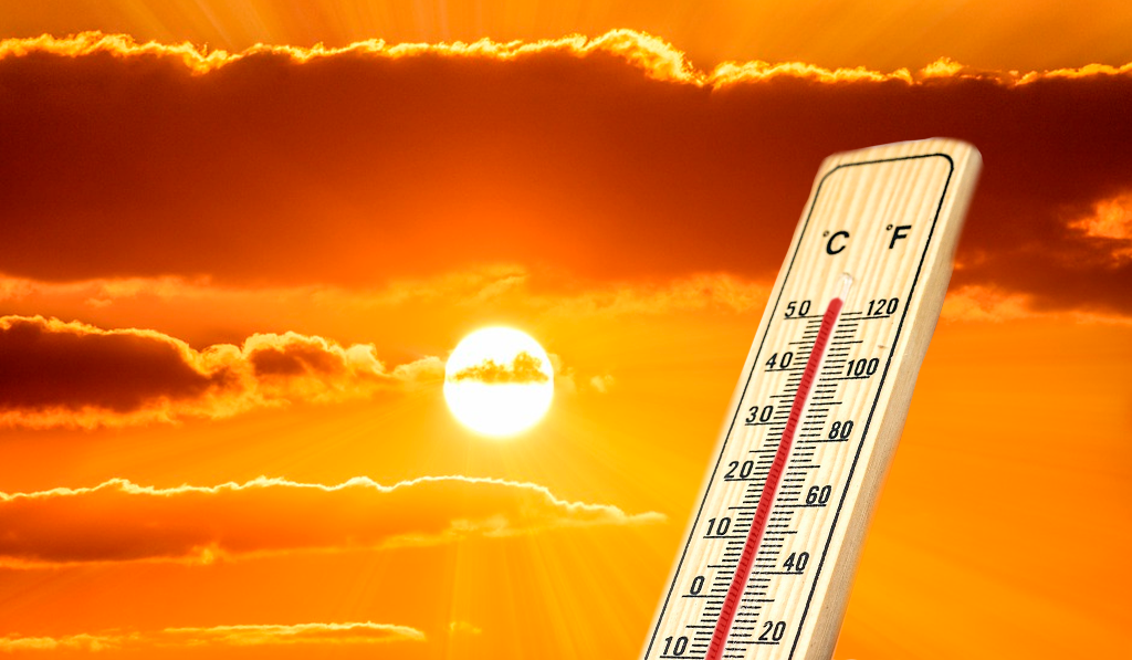 Un termómetro que indica alta temperatura. Al fondo un atardecer soleado.