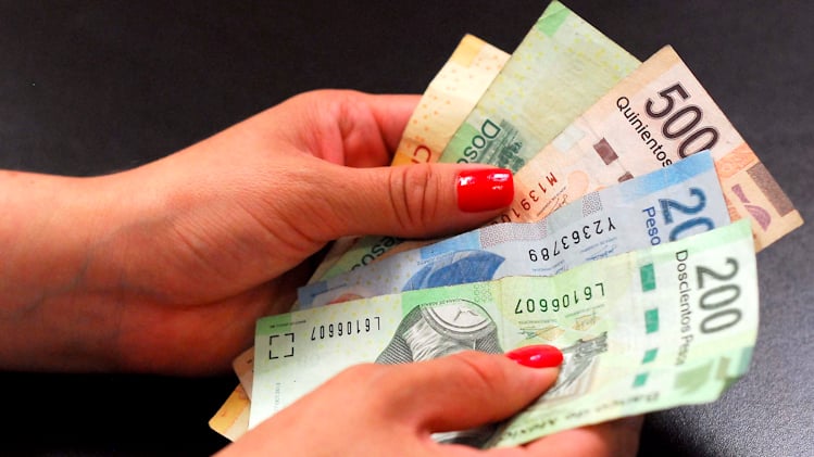 Manos sosteniendo billetes de pesos mexicanos.