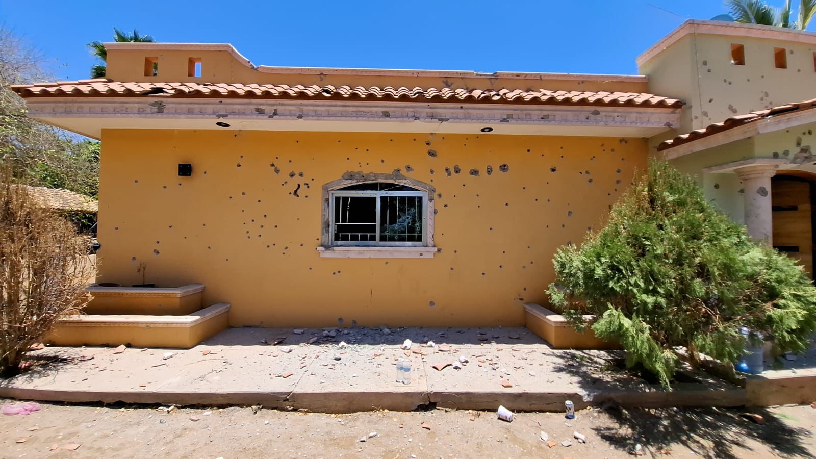 Casa de color amarillo con múltiples impactos de arma de fuego en toda la fachada.