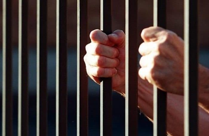 Persona sujeta las rejas de una celda en prisión