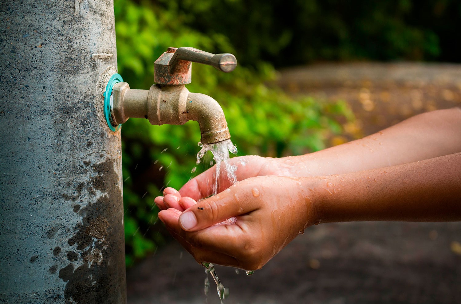 Grifo de agua abierto derramando agua y manos de una persona en el chorro de agua