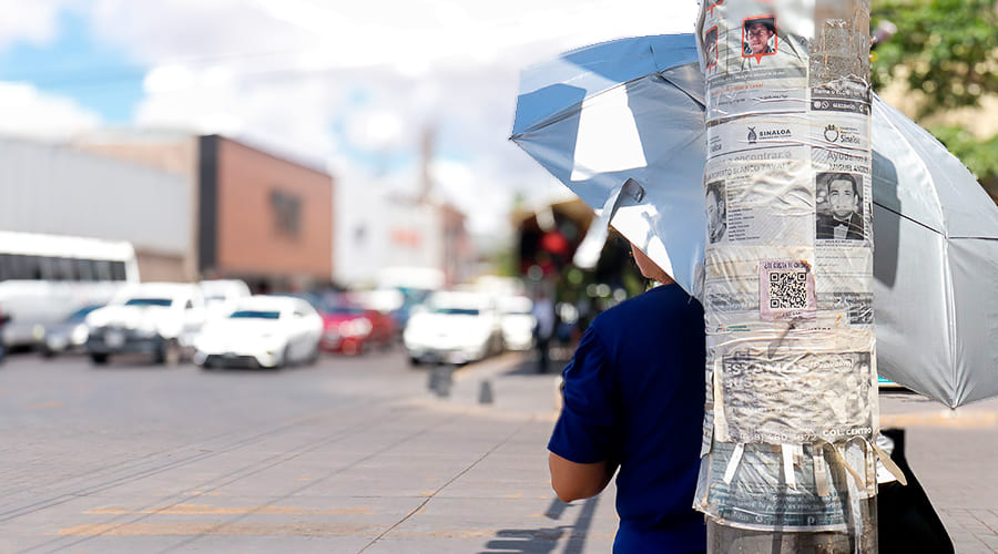 Mujer se protege del sol y calor bajo una sombrilla y detrás de un poste Clima Sinaloa