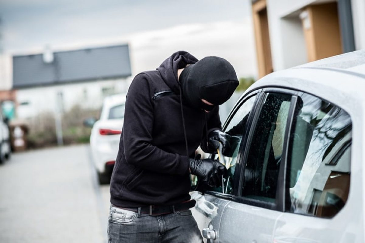 Persona con el rostro cubierto a lado de un carro tratando de abrirlo