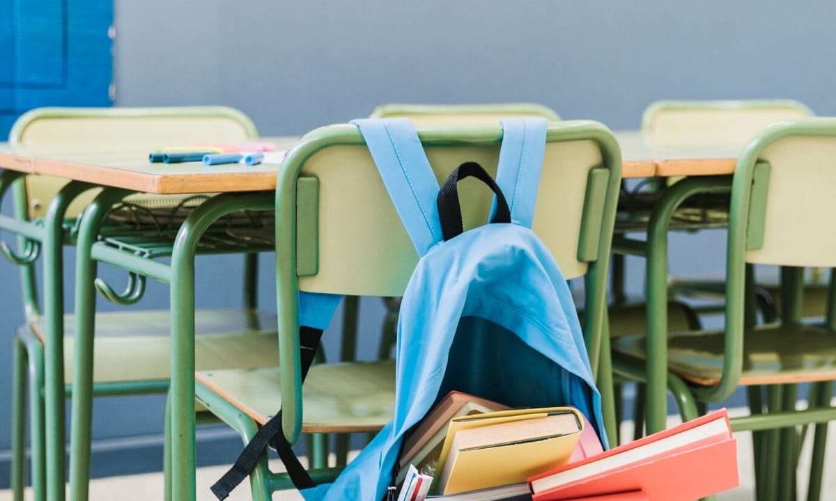 Salón de clases vacío y útiles escolares en una butaca.