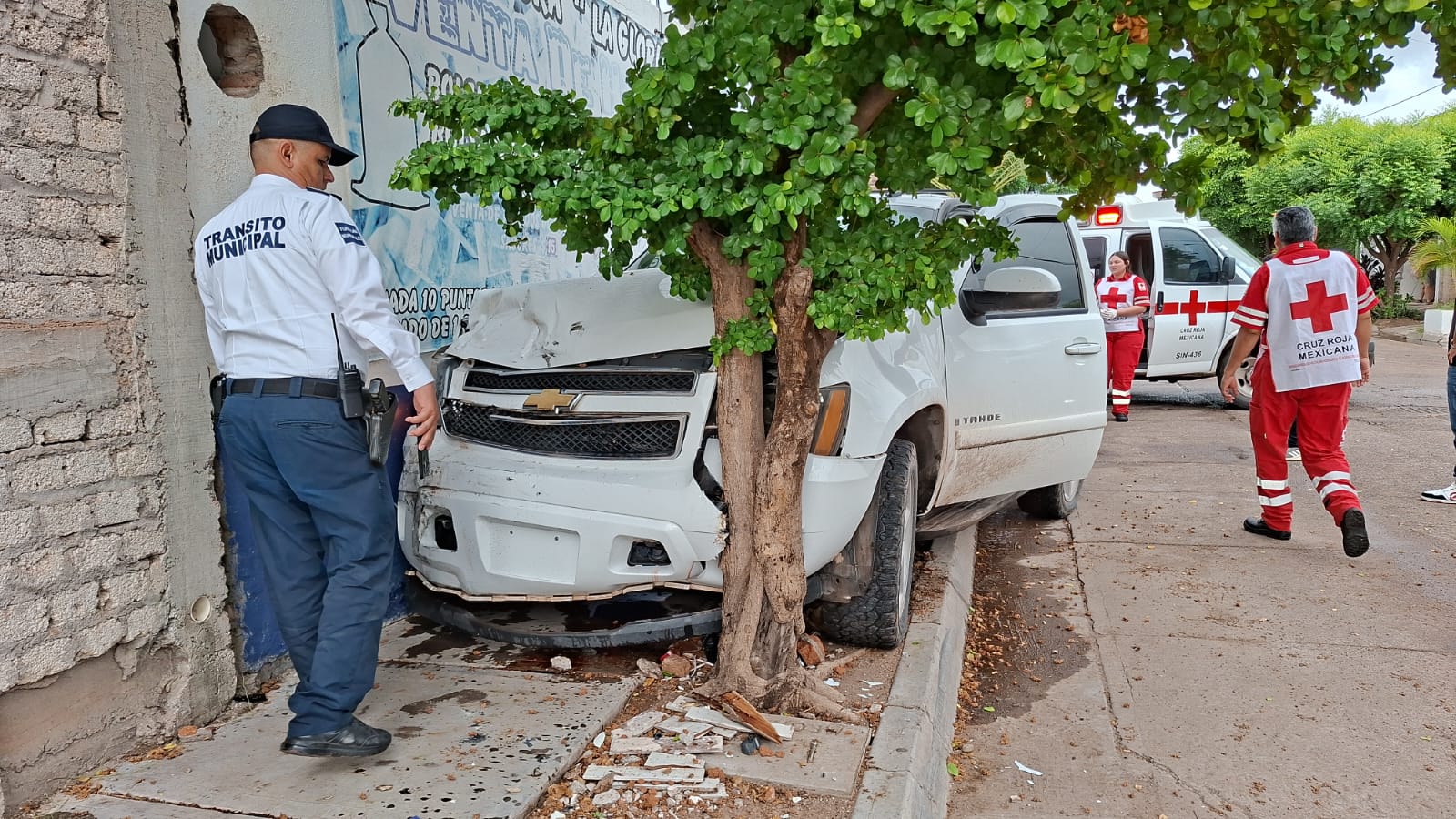 Camioneta Chevrolet Tahoe de color blanco estrellada contra un árbol y un muro.