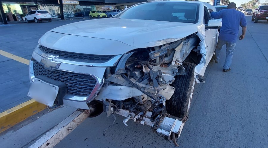 Un Chevrolet Malibú color blanco con la parte izquierda delantera destrozada después de un choque