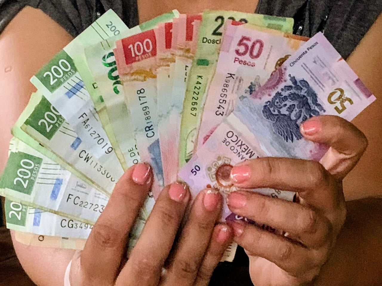 Persona sosteniendo con sus manos una cierta cantidad de billetes mexicanos