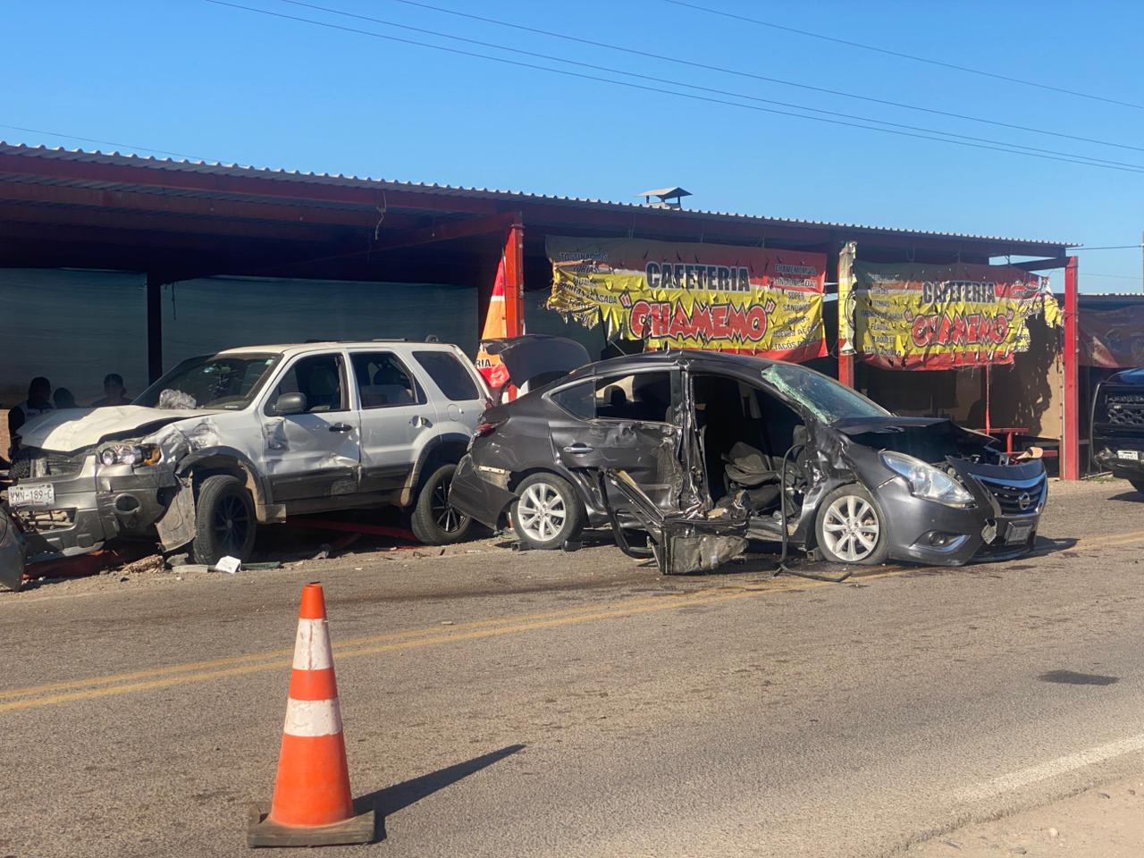 Dos carros chocados en una carretera, una camioneta blanca con la defensa delantera y el cofre dañados y un automóvil gris con el lado derecho completamente destruido por el impacto, alrededor conos de seguridad que protegen la zona del accidente.