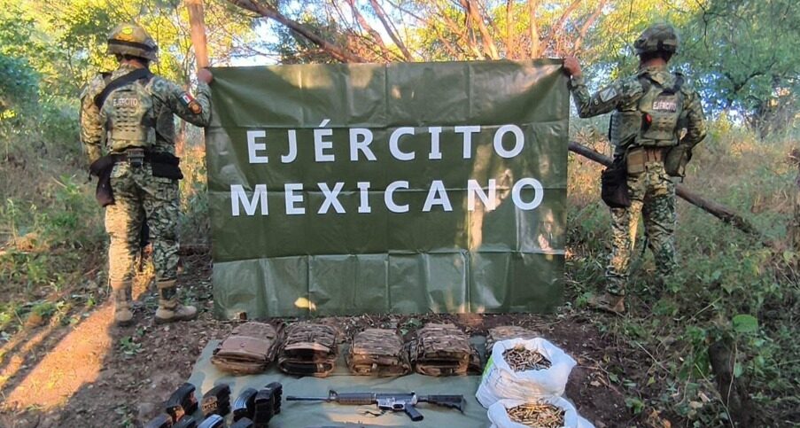 Dos elementos del ejército mexicano sosteniendo una lona junto a droga y armas aseguradas en el piso en San Ignacio