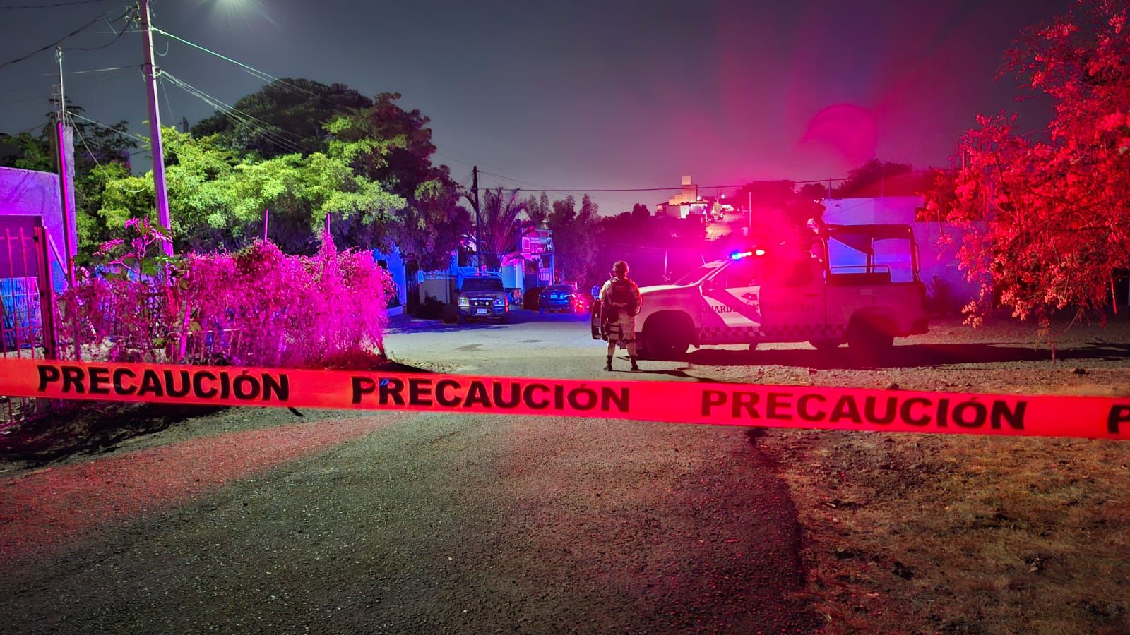 Cinta policial amarilla y al fondo elementos de la Guardia Nacional en una camioneta