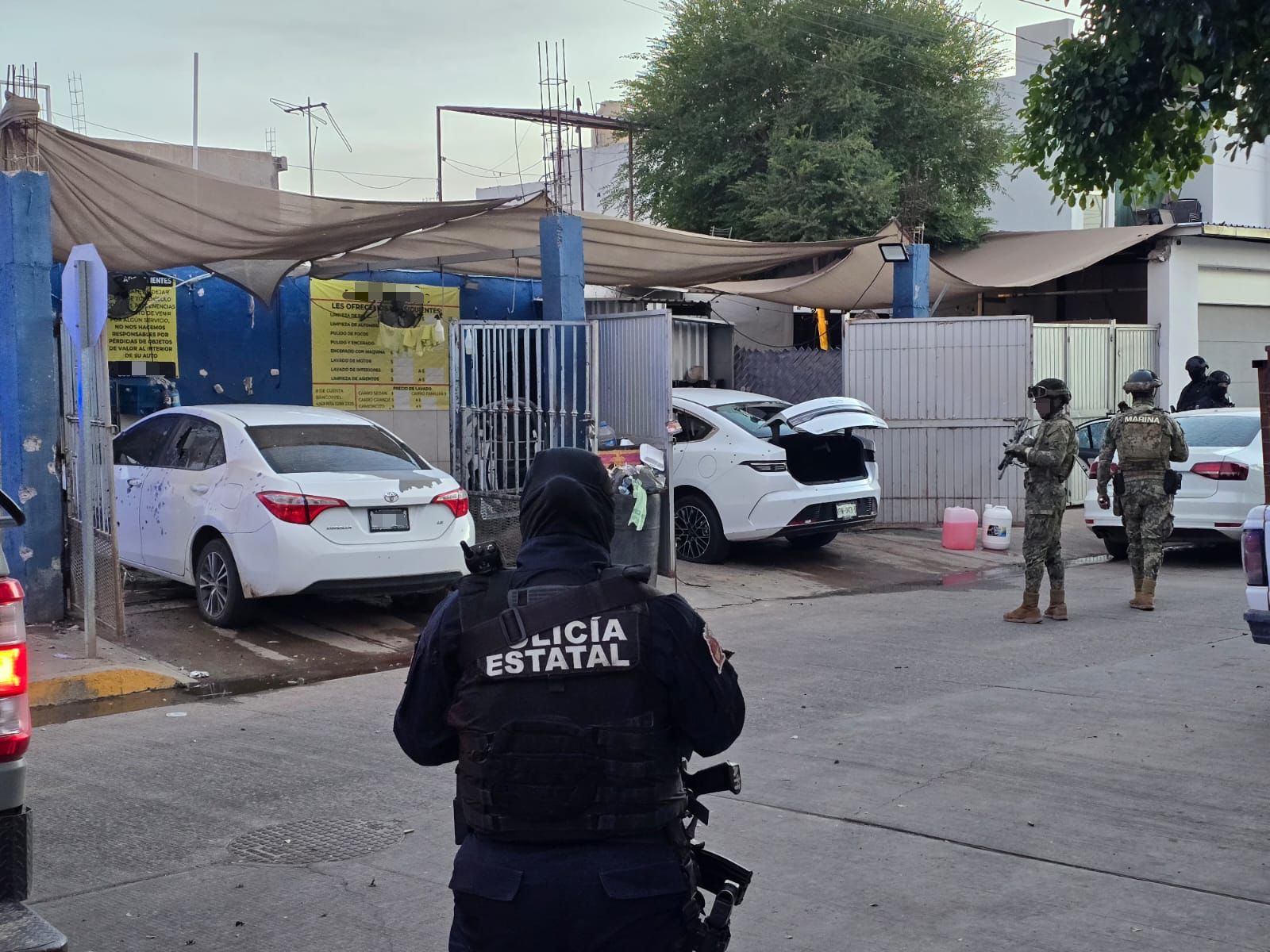 Policías afuera de un autolavado donde hay dos carros baleados