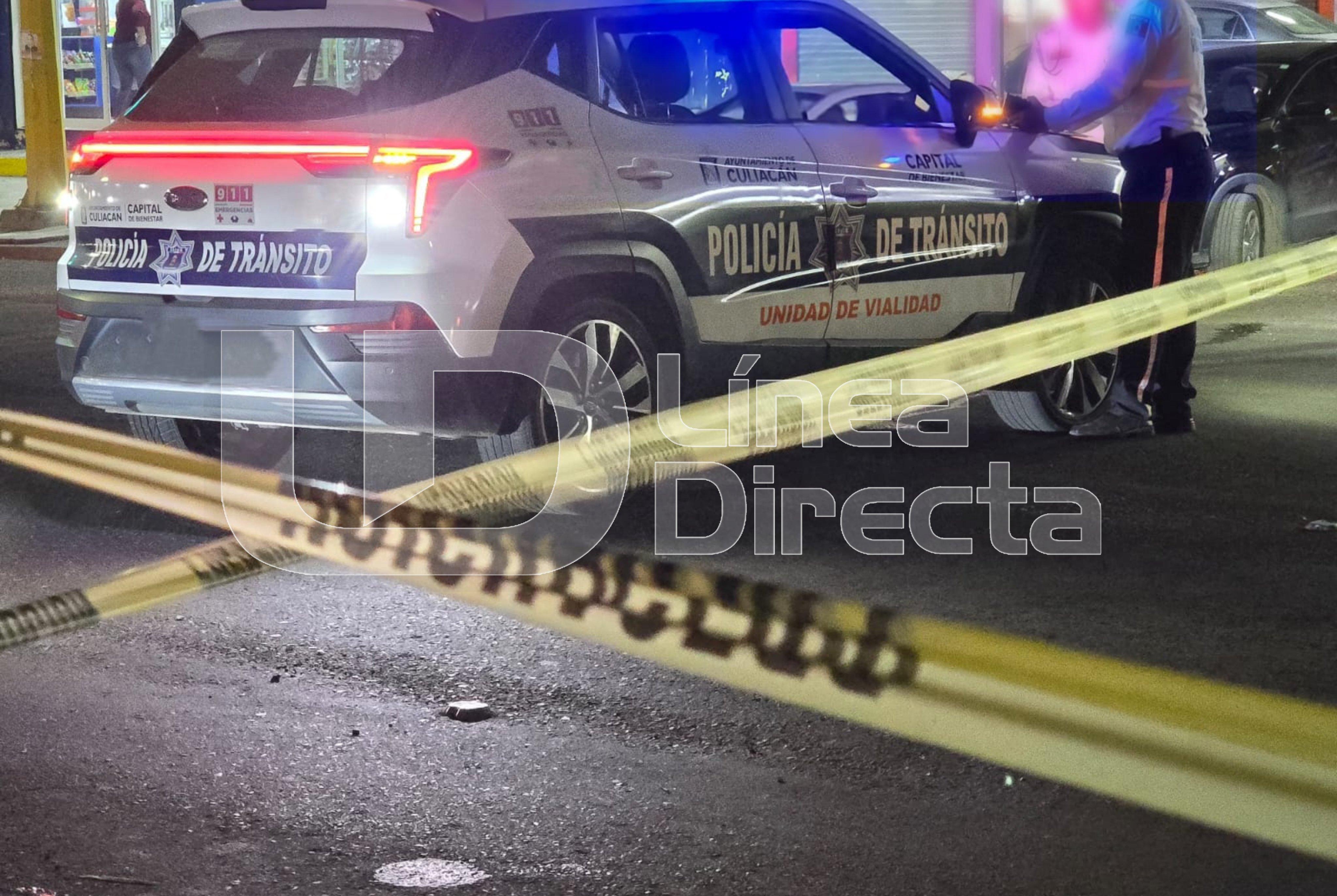 Unidad de transito de Culiacán estacionada en la calle y un elemento debajo de la unidad, se muestra también cinta de precaución.