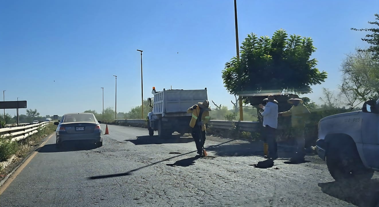 Carretera México 15 en trabajos de bacheo, se ve a trabajadores laborando aplanando el terreno y a autos transitando por un costado de los baches