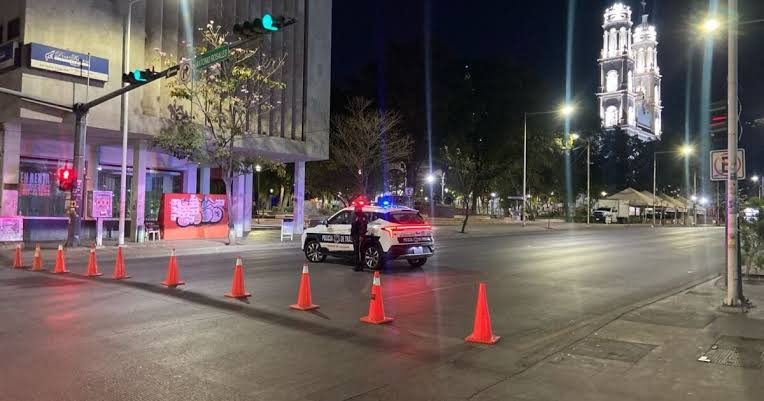 Vialidad cerrada con conos naranjas y un elemento policial junto a una unidad