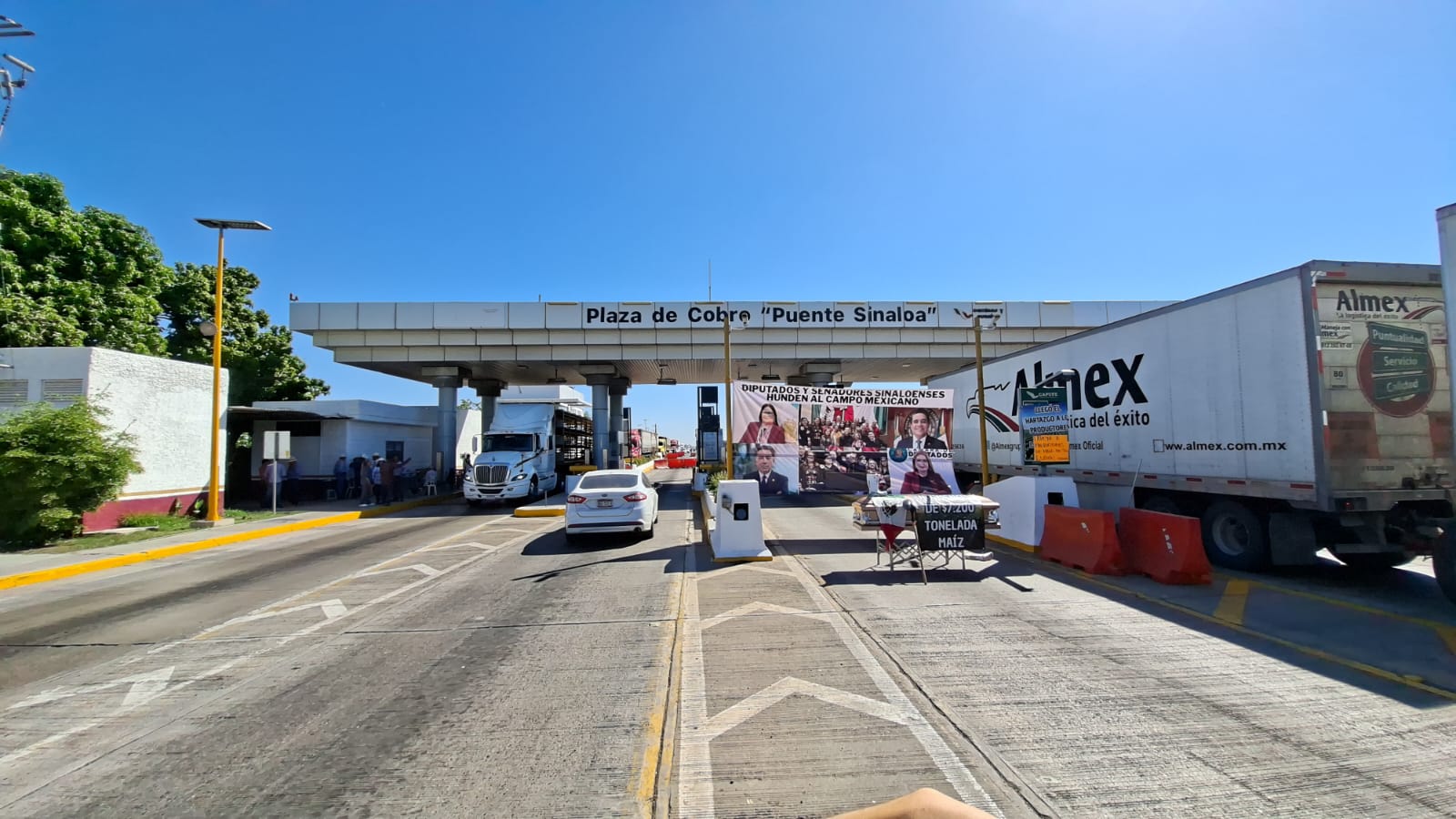 Caseta de Sinaloa intervenida por campesinos de Sinaloa en forma de protesta, donde se ven dos tráilers tapando entradas y salidas, y amarrado a dos postes, una lona donde con una leyenda que muestra la inconformidad de los campesinos con respecto a los precios y atención que se les ha dado