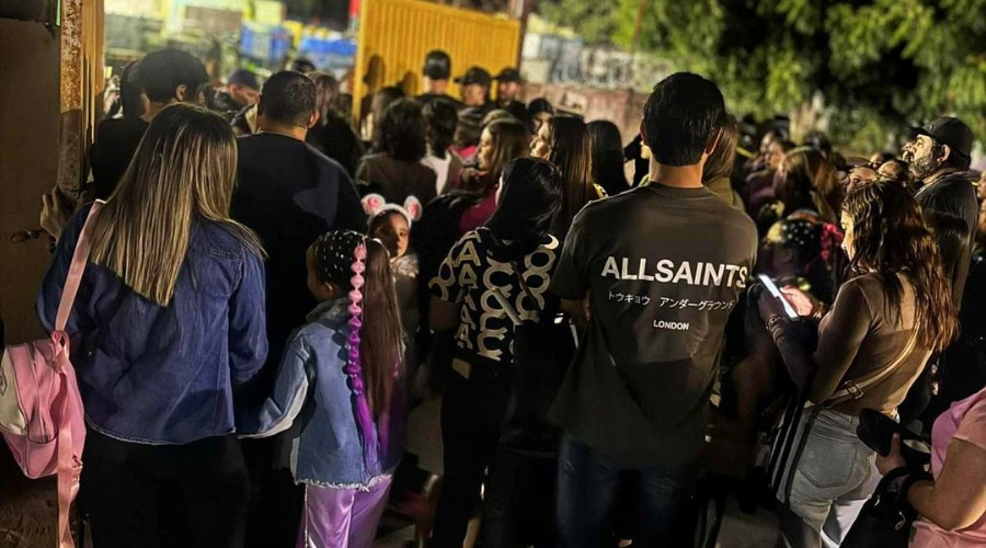 Padres de familia y niñas de espaldas intentando ingresar a un recinto pero se ven detenidos en la puerta de acceso