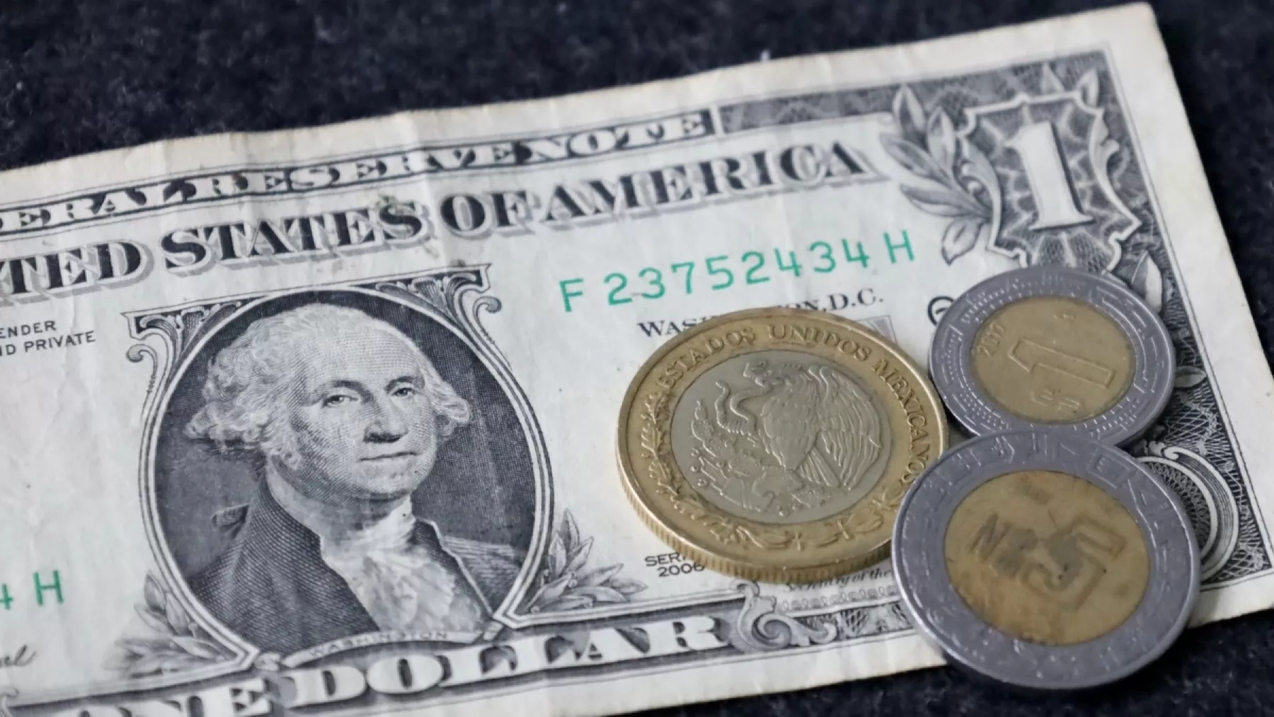 Imagen de un dólar con 3 monedas de pesos mexicanos en denominación de 10, 5 y 1 pesos.