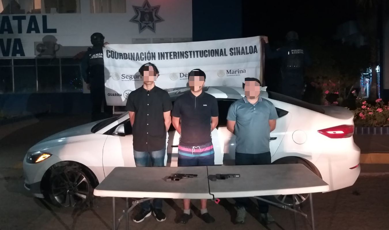 Elementos sosteniendo una lona detrás de un carro blanco y 3 personas con las manos en sus espaldas, en una mesa está lo asegurado
