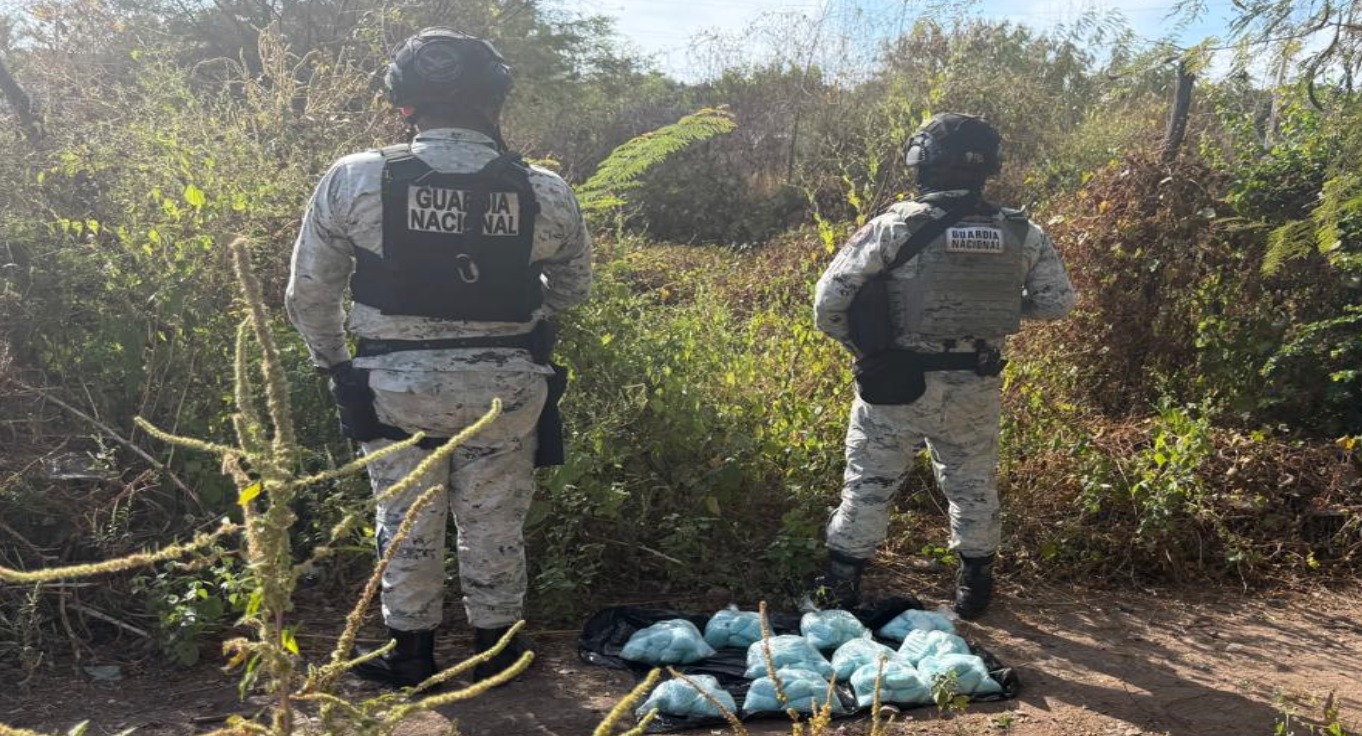 Dos elementos de la Guardia Nacional de espaldas, localizados en un monte y debajo de ellos la droga asegurada en el operativo